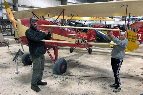 Photo of a father and teen holding up a large model airplane modeled on the plane they are standing in front of.